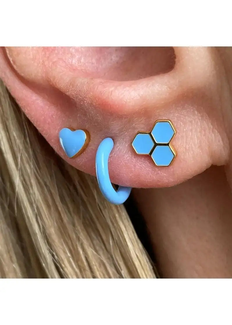 Close-up of ear with three blue earrings: hexagon stud, heart stud, and hoop.