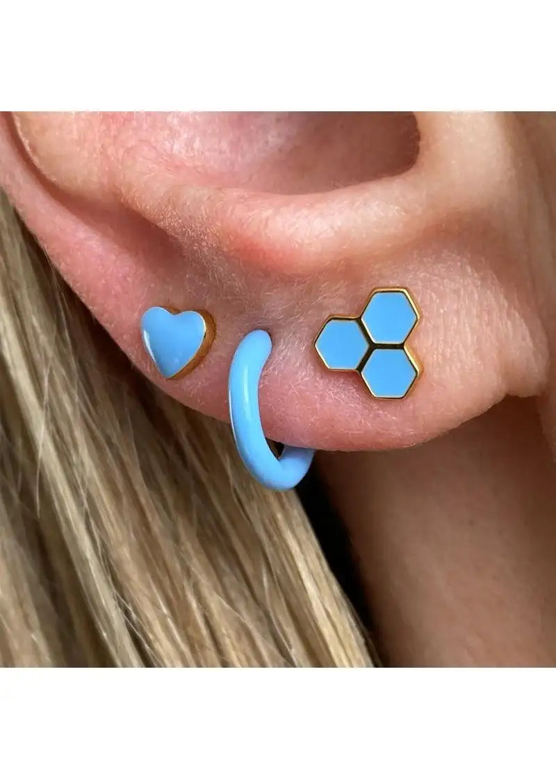 Close-up of ear with three blue earrings: hexagon stud, heart stud, and hoop.