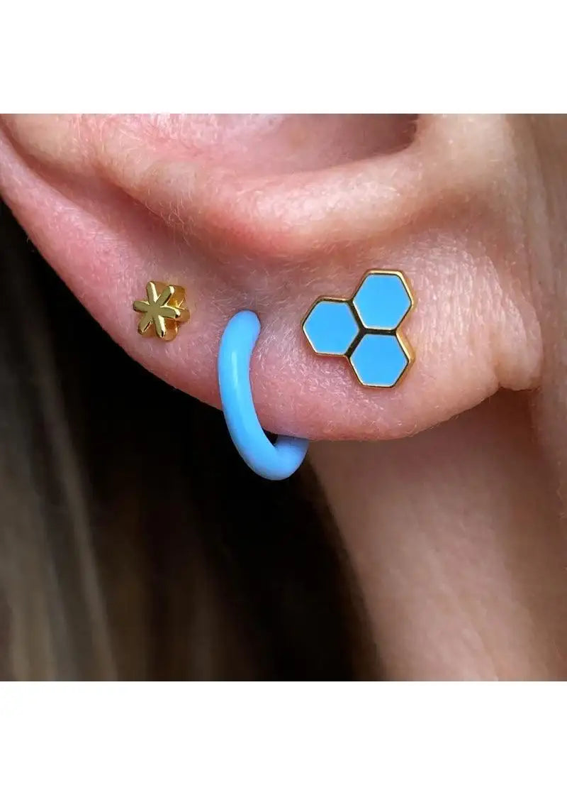 Close-up of ear with gold flower stud, blue hoop earring, and blue hexagon stud earrings