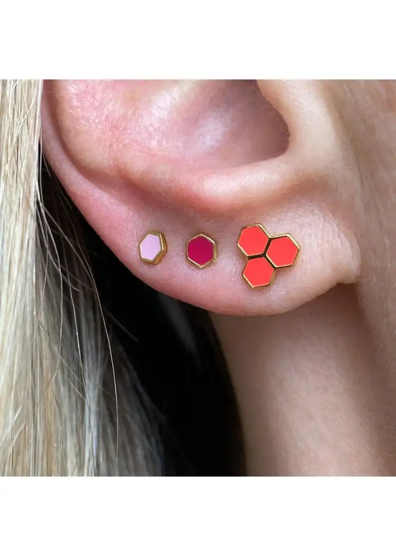 Close-up of ear with three geometric stud earrings in hexagon and honeycomb shapes, gold edges