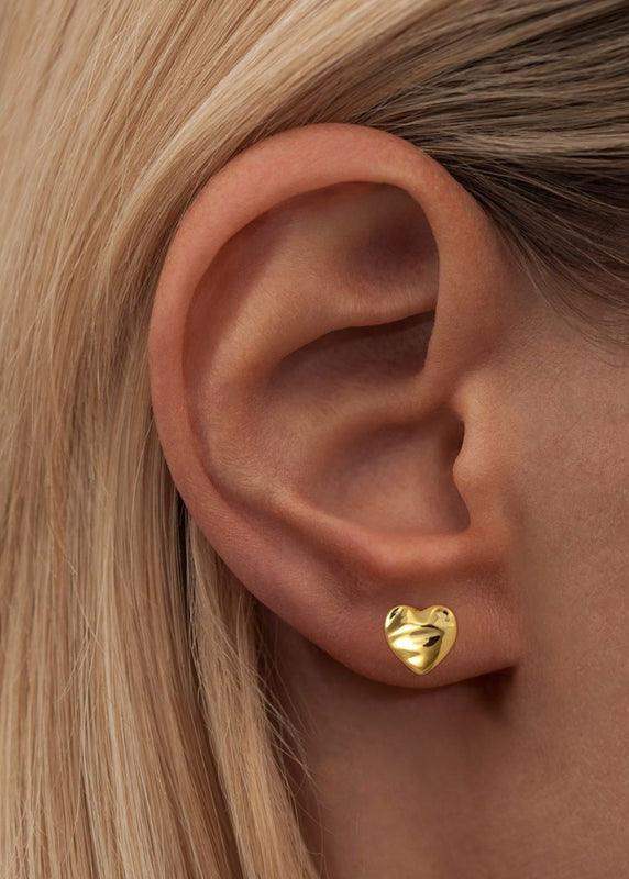 Gold melted heart stud earring worn on ear, minimalist and modern jewelry design.