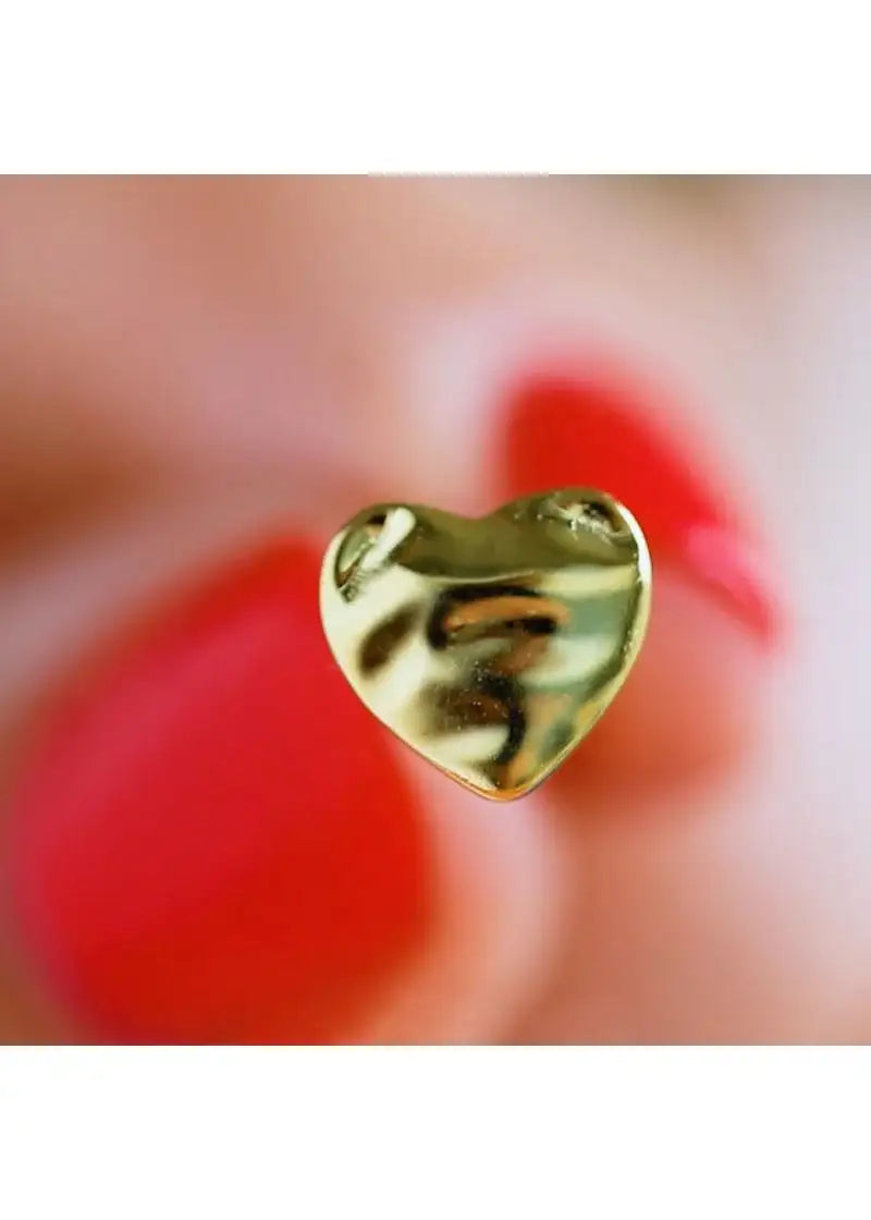 Close-up of a gold melted heart stud earring held between fingers with red nail polish.