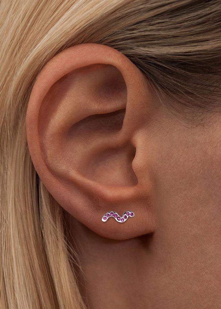 Snaky silver earring with pink gemstones worn on ear, modern minimalist jewelry