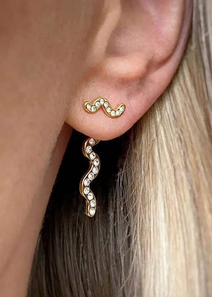 Close-up of ear wearing gold-tone, wavy, crystal-studded snake earrings