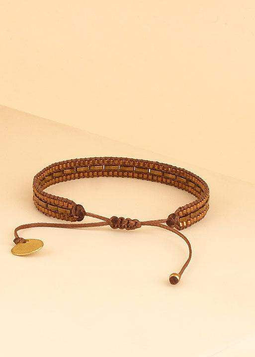 Brown beaded adjustable bracelet with gold charm on neutral background