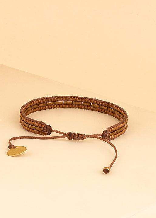 Brown beaded adjustable bracelet with gold charm on neutral background
