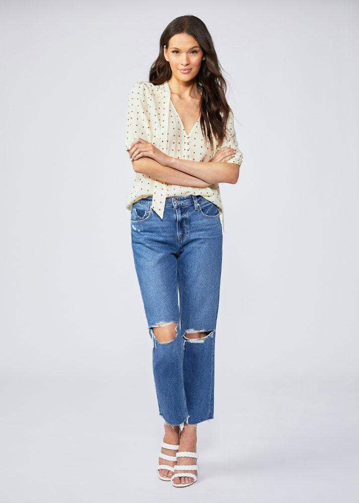 Woman wearing straight leg ripped blue jeans and polka dot blouse, white heels