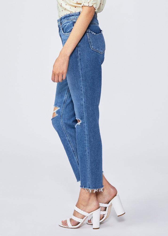 Woman wearing high-waisted straight leg distressed blue jeans with raw hems and heels