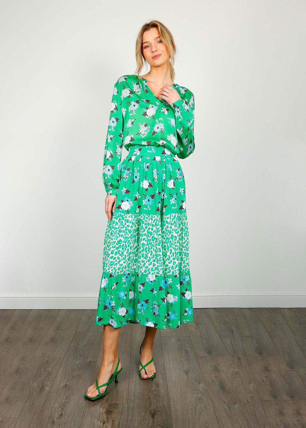 Woman wearing green floral and animal print midi skirt and blouse set, standing indoors