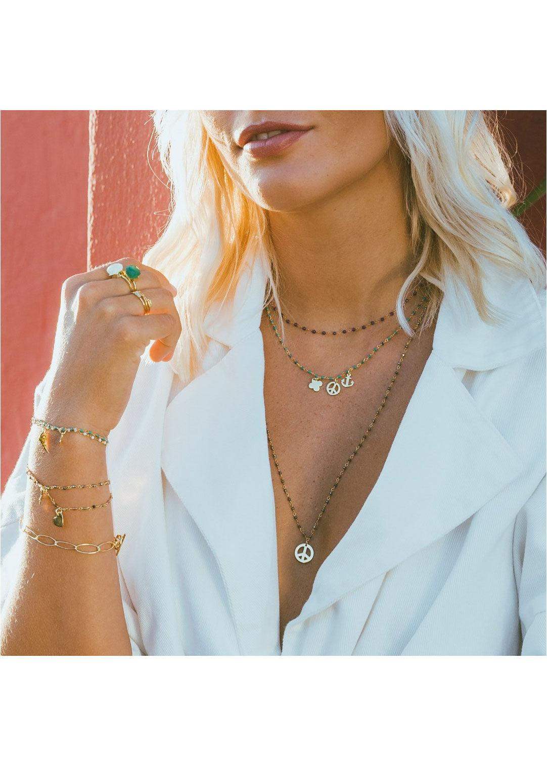 Layered gold pyrite necklaces with symbol charms worn by woman in white blazer, boho jewelry style