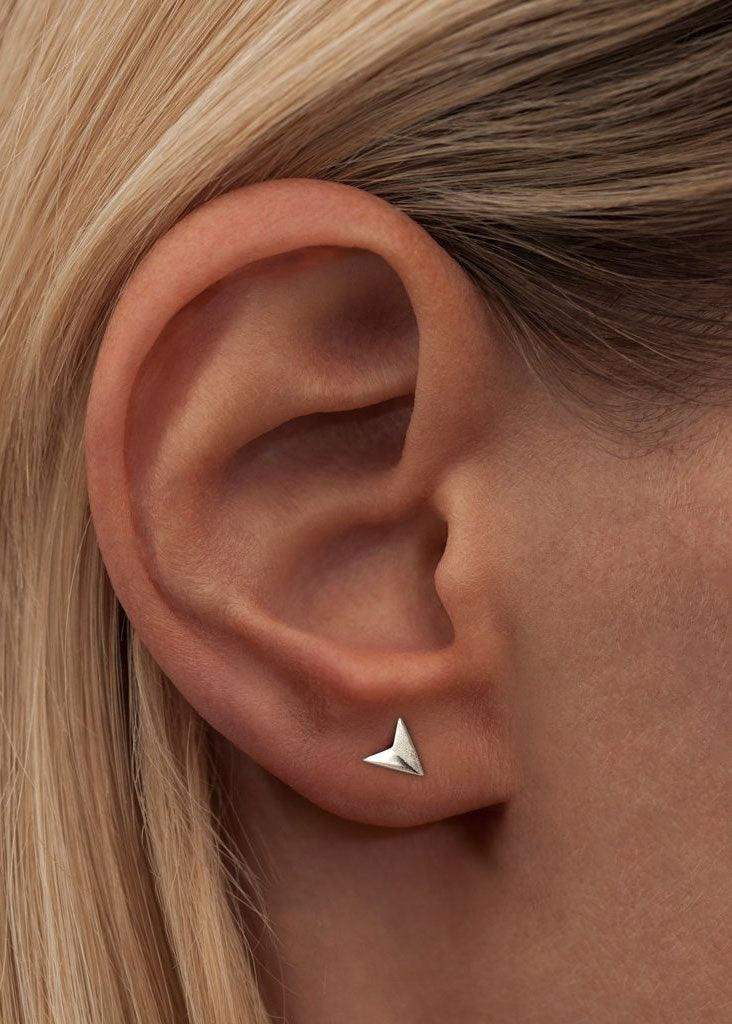 Minimalist silver paper plane stud earring worn on ear, close-up view