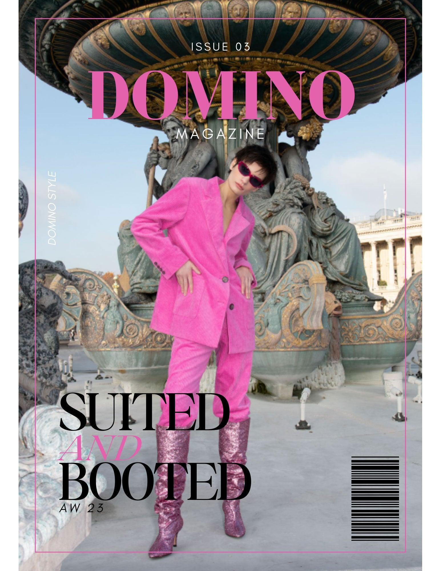 Fashion model in bold pink suit and glitter boots poses by ornate fountain, magazine cover style.