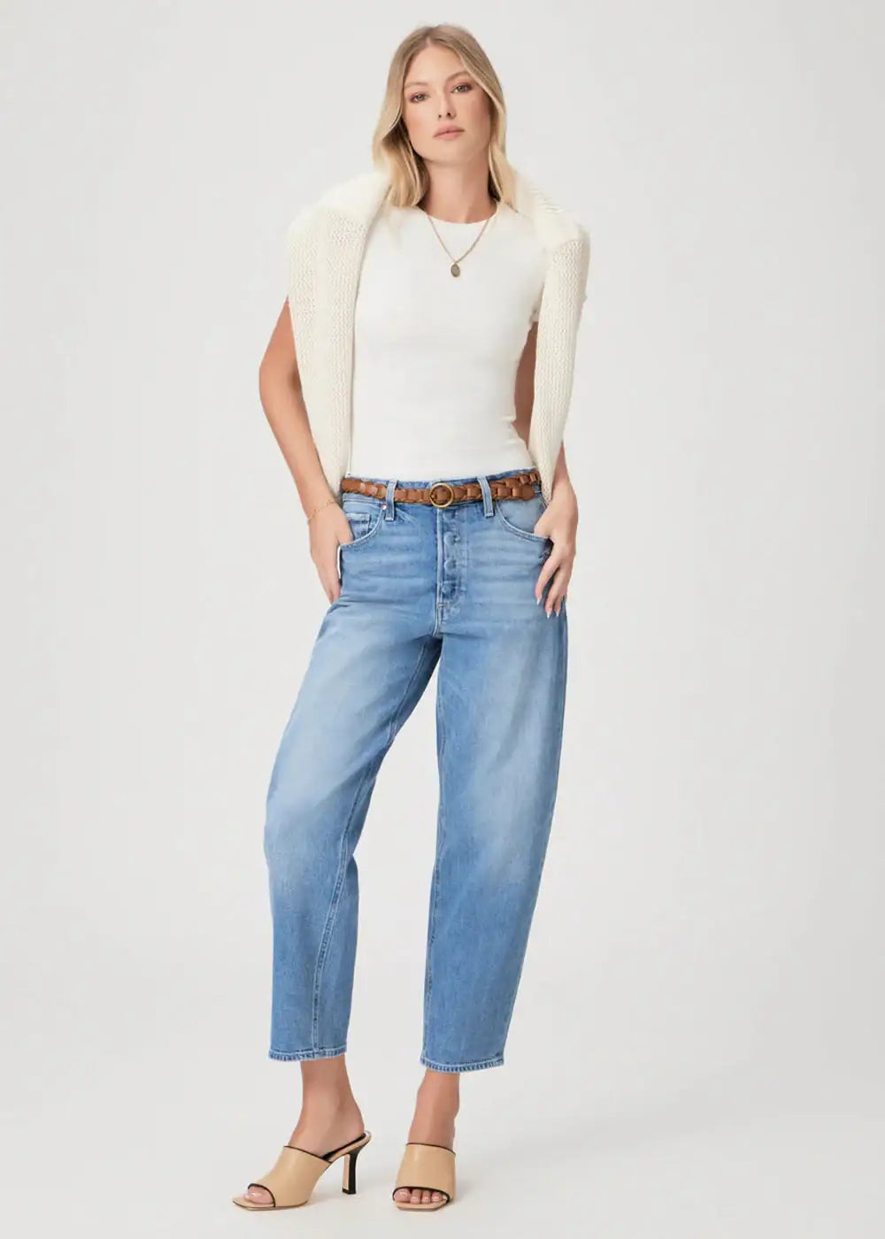 Woman in white top, relaxed blue jeans, beige knit sweater, and heeled sandals