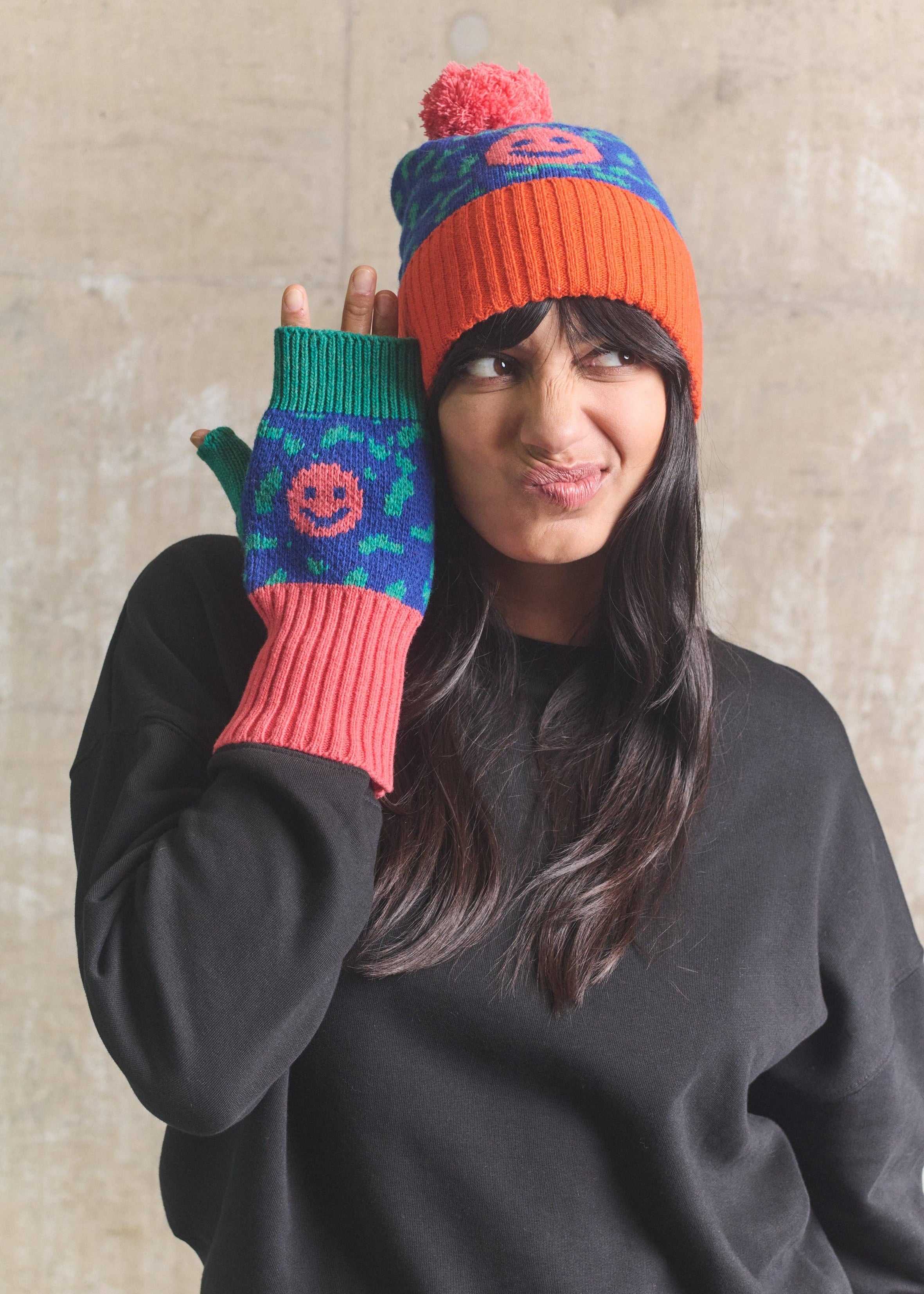 Person wearing colorful knit hat and gloves against a textured wall.