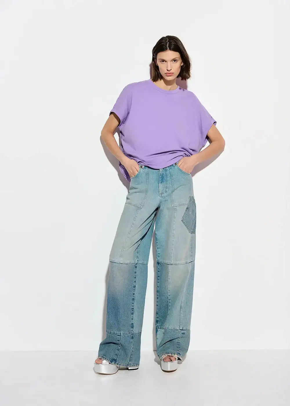 Woman in a loose lilac t-shirt and wide-leg patchwork jeans with platform sandals