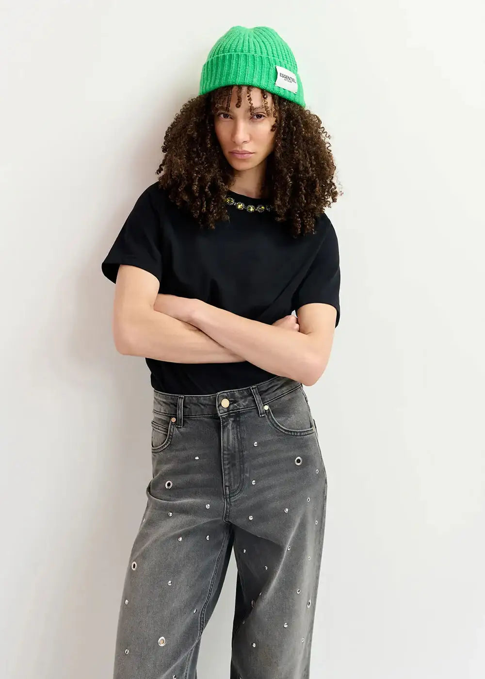 Woman wearing green beanie, black embellished t-shirt, and studded wide-leg grey jeans