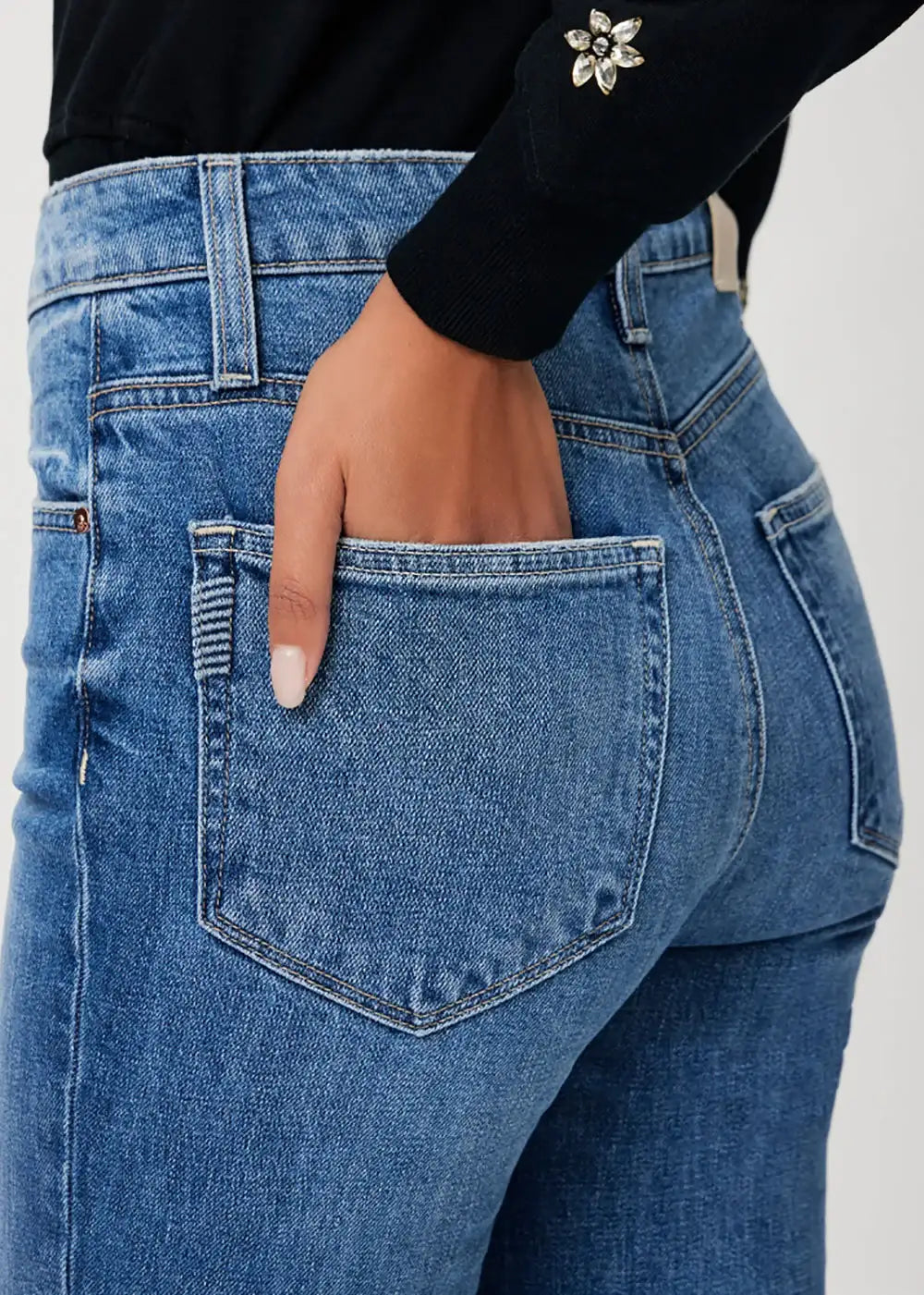 Close-up of blue denim jeans back pocket with hand, black sweater with jeweled cuff detail